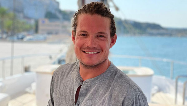 Below Deck's Gary King smiles in grey linen shirt while posing on yacht